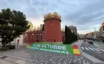 FOTOGRAFÍA. FIGUERAS, 12 OCTUBRE DE 2026. La instantánea retrata los exteriores de la plaza que da acceso a la Torre Galatea del Teatro-Museo Dalí de Figueras, donde militantes y simpatizantes de la formación patriota Vox han desplegado una imponente lona de color verde de varios metros de longitud que reza en letras blancas capitulares «12 DE OCTUBRE. FIESTA NACIONAL», flanqueada en sus dos extremos por los colores de la enseña nacional de España. Al fondo se recorta el singular edificio de color granate coronado por sus emblemáticos huevos gigantes y la cúpula geodésica acristalada diseñada por el genio surrealista Salvador Dalí, contrastando con la calzada limpia y semivacía de la avenida adyacente durante el amanecer de este lunes. La acción de guerrilla pacífica enmarcada en la declaración institucional del diputado Alberto Tarradas Peneque escenifica la resistencia cultural de la formación verde en el corazón del independentismo de cara a las próximas elecciones del 29 de noviembre, proyectando un mensaje nítido de soberanía, orgullo e indisoluble unidad nacional. Lasvocesdelpueblo (Ñ Pueblo).