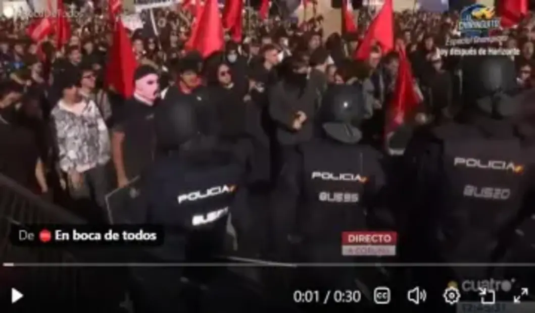FOTOGRAFÍA. LA CORUÑA, 21 DE OCTUBRE DE 2026. Despliegue de los furgones de la Unidad de Intervención Policial de la Policía Nacional para contener a miles de contramanifestantes separatistas y de ultraizquierda que ocuparon la plaza de María Pita para intentar impedir el acto político de Vox en pleno periodo electoral. Captura de pantalla de una emisión en directo del programa «En boca de todos» de la cadena Cuatro. La imagen muestra un primer plano de un nutrido grupo de manifestantes de ultraizquierda y separatistas, muchos de ellos encapuchados o con el rostro cubierto, enarbolando banderas rojas y secesionistas gallegas. Frente a ellos, varios agentes de la Policía Nacional equipados con cascos y chalecos antibalas forman una barrera de contención de espaldas a la cámara. Lasvocesdelpueblo (Ñ Pueblo)